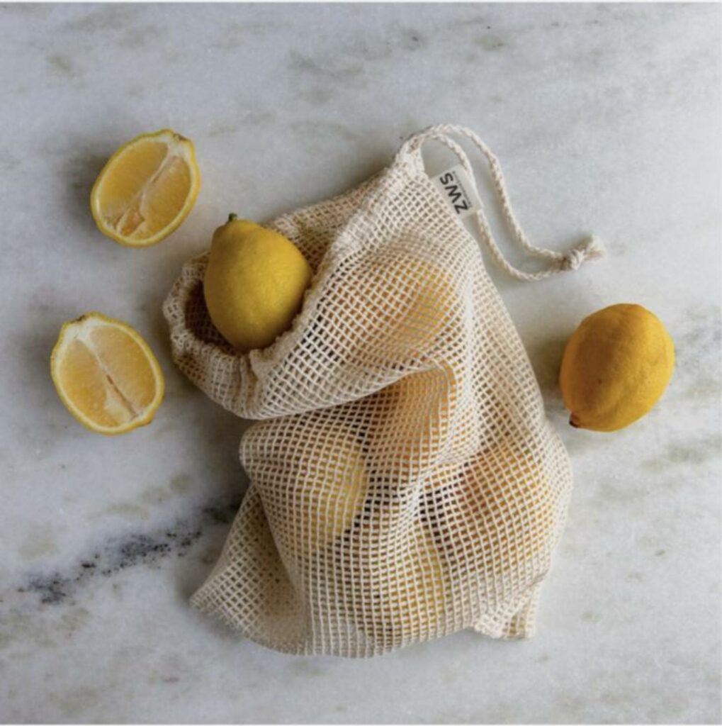 A beige mesh cotton bag containing lemons, with cut lemons shown alongside.