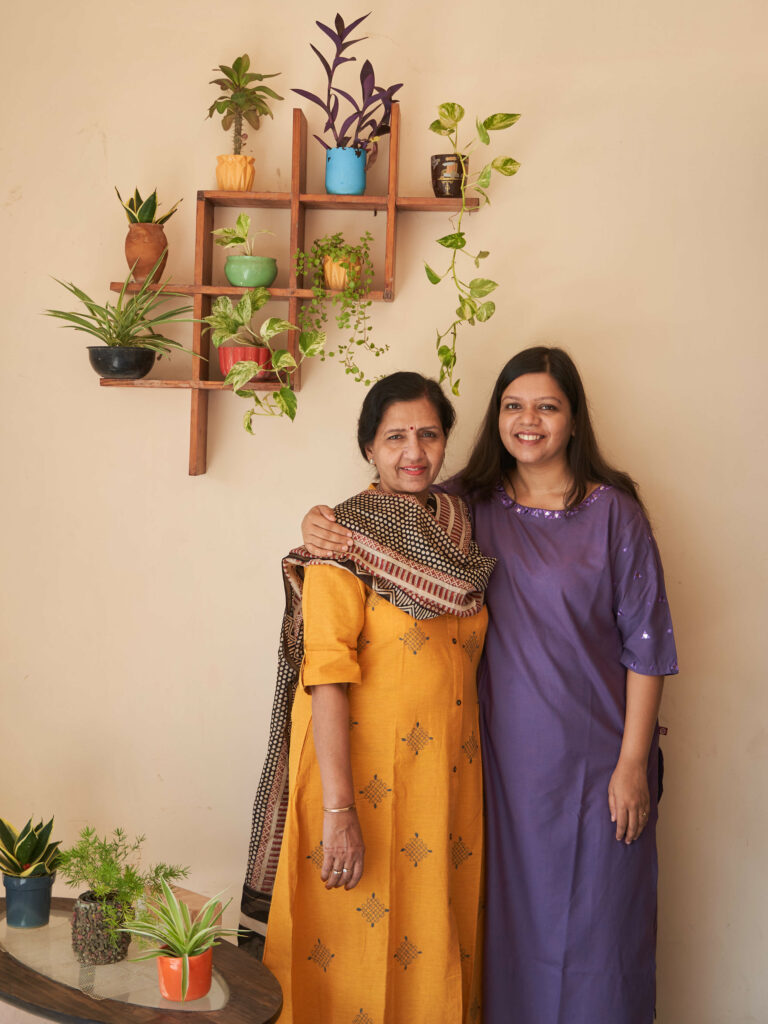 Two women pose in front of a beige wall.